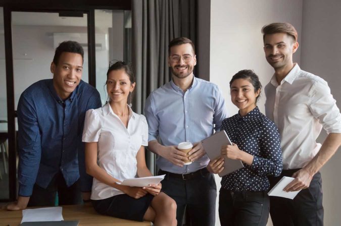 Five employees posing for a group photo in the workplace