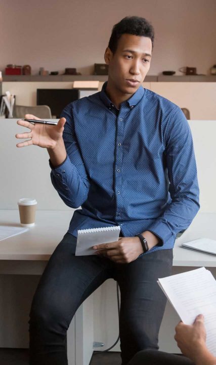 a man leaning on a desk and speaking with another person